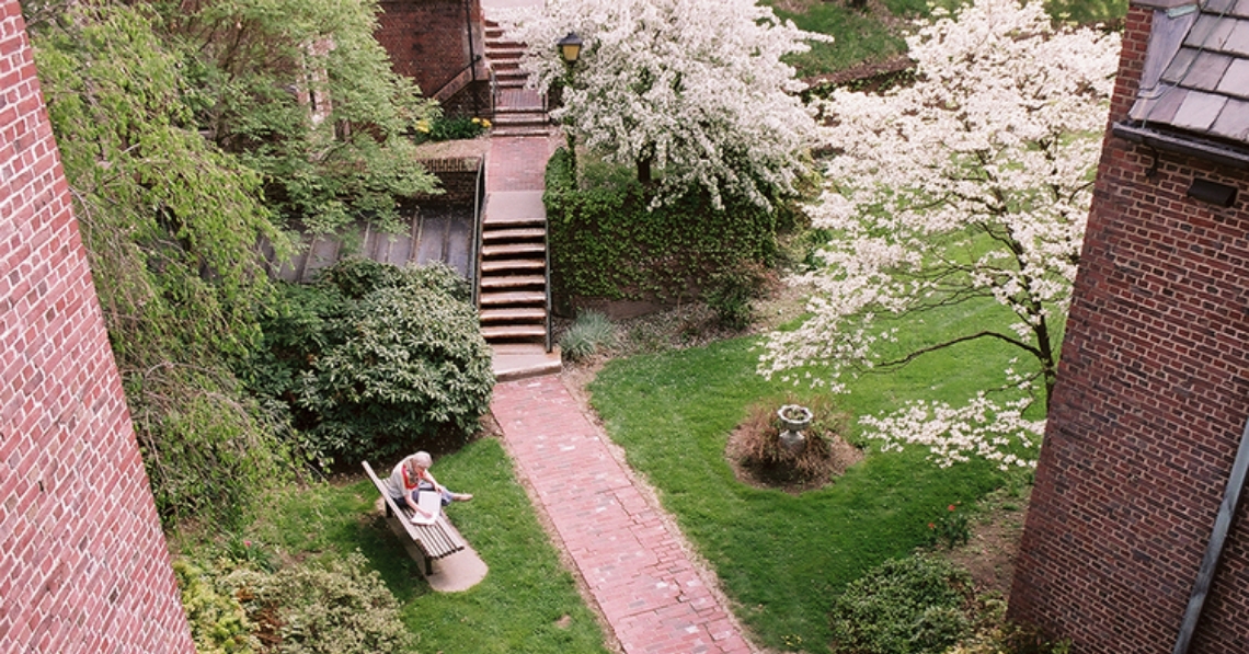 One of the  BA residents reads in foyer with blooming Red Buds in courtyard in spring.